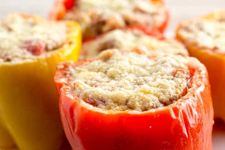 Five pressure cooker stuffed peppers topped with parmesan on white plate.