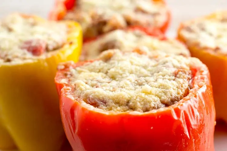 Five pressure cooker stuffed peppers topped with parmesan on white plate.