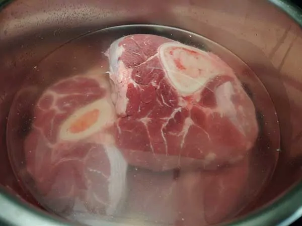 Uncooked beef shanks in pot covered with water.