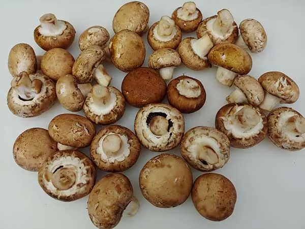 Baby bella mushrooms on white cutting board.