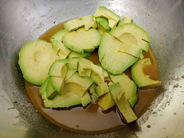 Chopped avocados and vinaigrette in mixing bowl.