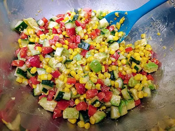 Red peppers, corn, and cucumbers combined with avocados in mixing bowl.