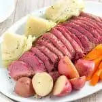 sliced corned beef brisket on serving platter with cabbage, potatoes, and carrots.