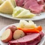 sliced corned beef brisket on small plate with cabbage, potatoes, and carrots with platter in background.