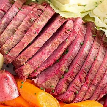 sliced corned beef brisket on serving platter with cabbage, potatoes, and carrots.