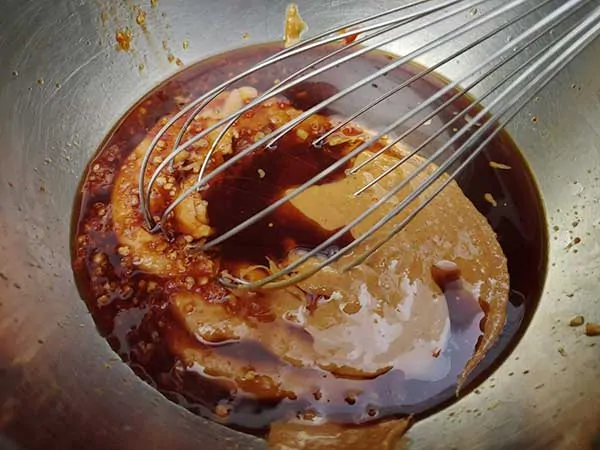 Peanut butter, soy sauce, and sesame oil in bowl with whisk.
