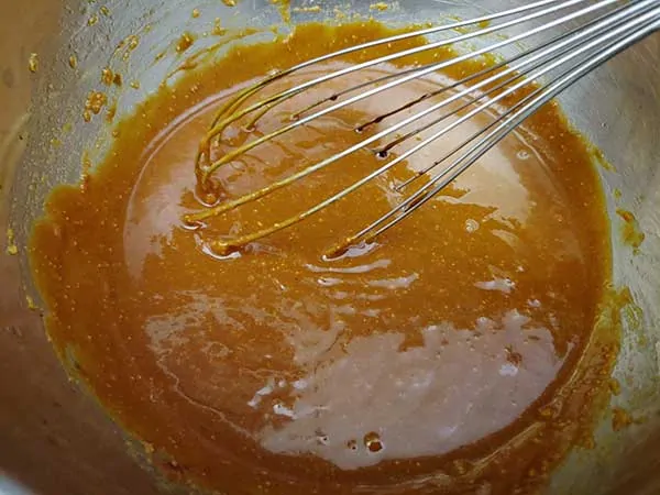 Spicy peanut sauce in mixing bowl with whisk.