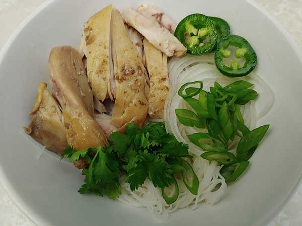 Chicken, herbs, and onions on rice noodles in white bowl.