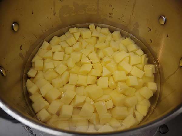 Chopped gold potatoes covered in water in pot.