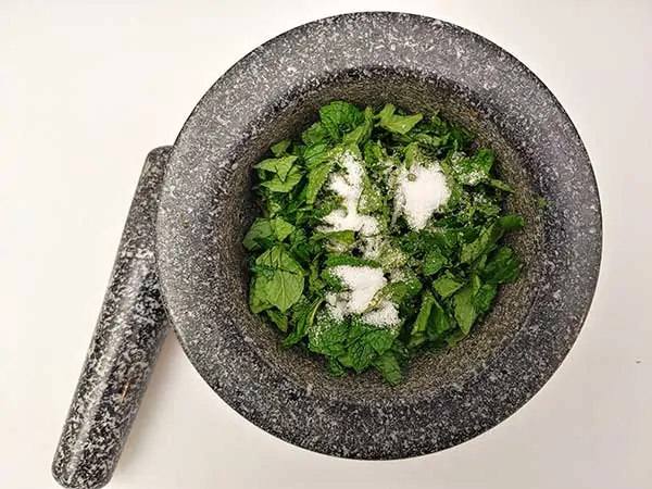 Mint leaves in mortar and pestle topped with salt.