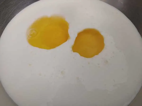 Two eggs in bowl of buttermilk.