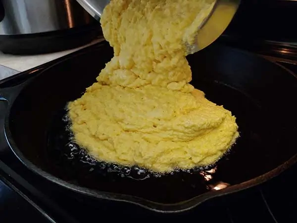 Pouring cornbread batter into hot cast iron skillet.