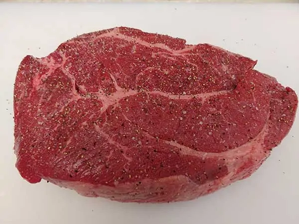 Uncooked chuck roast seasoned with salt and pepper.