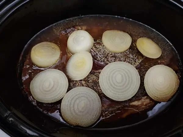 Pot roast cooking in Crock Pot with sliced onions.