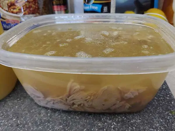 Shredded turkey and stock in plastic container.