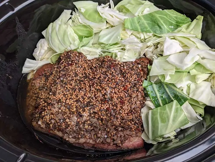 Cooked corned beef in slow cooker with raw cabbage.