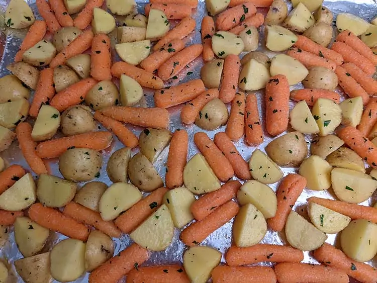 Seasoned baby carrots and potatoes on baking sheet.