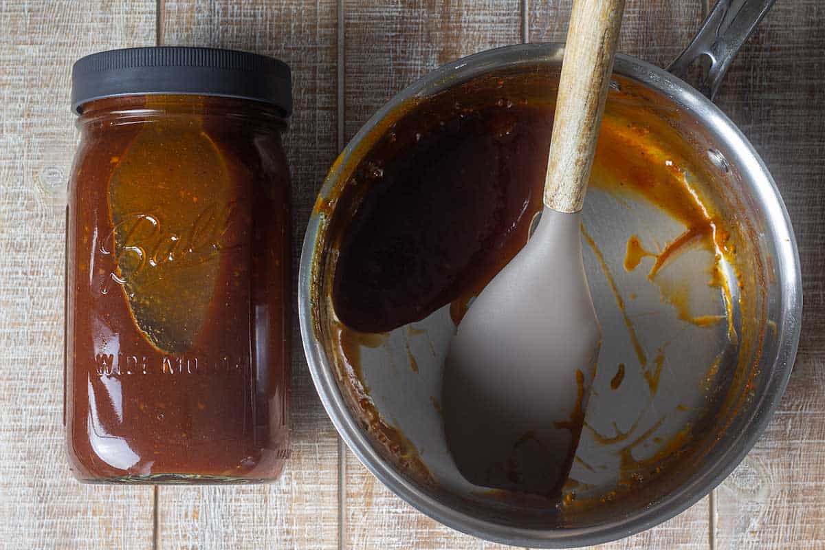 Mason jar full of homemade BBQ sauce next to an empty saucepan