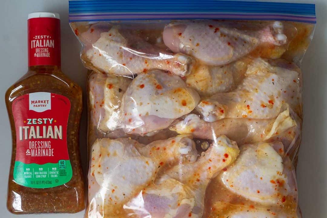 Chicken marinating in a storage bag next to a bottle of Zesty Italian dressing