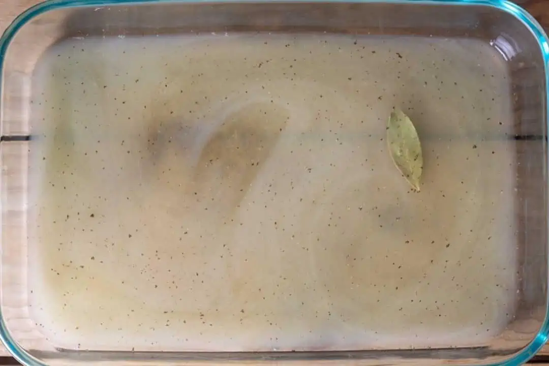 Pyrex dish with chicken broth, spices, and a bay leaf