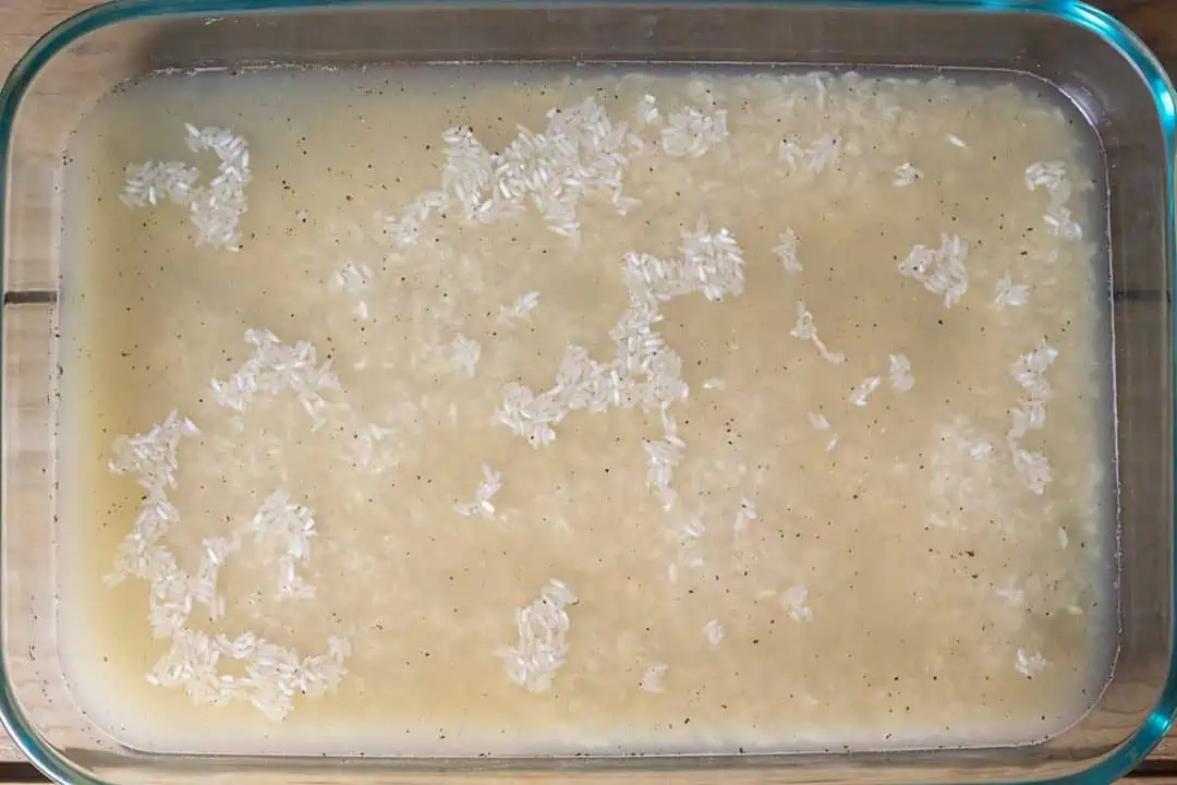 Uncooked white rice and chicken broth in Pyrex dish