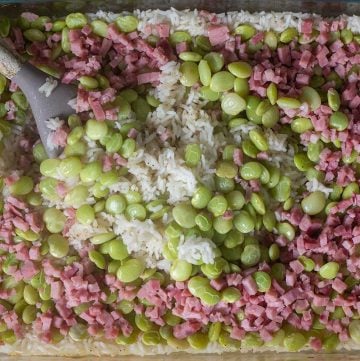 mixing the layers of ham and baby lima bean rice bake in Pyrex dish