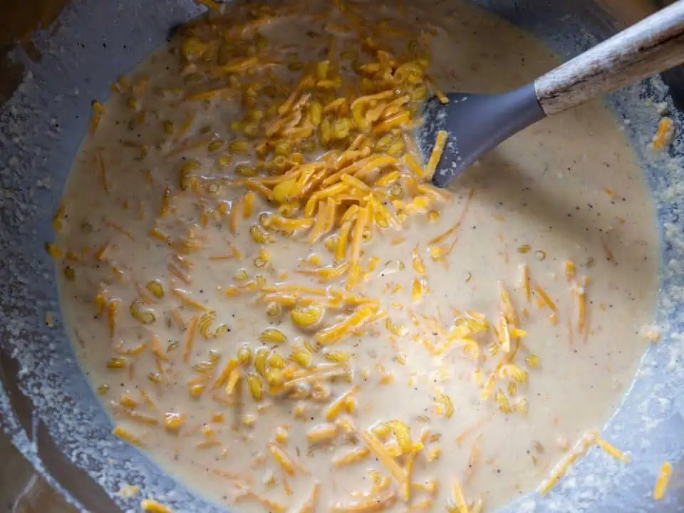 mac and cheese ingredients being mixed with spatula in large mixing bowl.