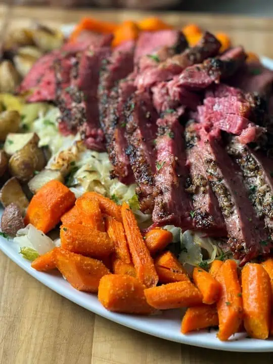 Sliced pressure cooker corned beef on a bed of cabbage, carrots, and potatoes bed.