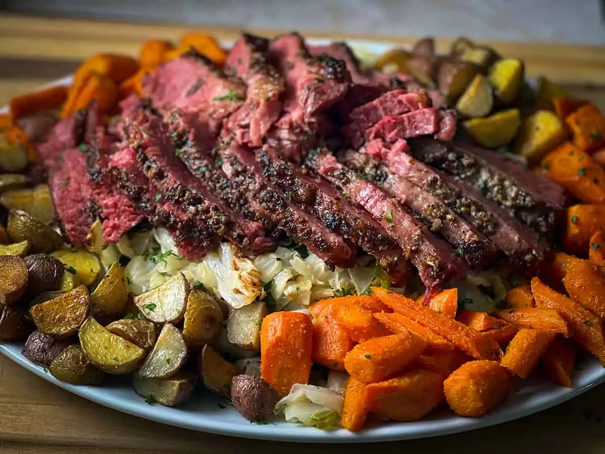 Sliced pressure cooker corned beef on a bed of cabbage, carrots, and potatoes.