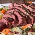 Sliced pressure cooker corned beef on a bed of cabbage, carrots, and potatoes on a white plate with wooden background