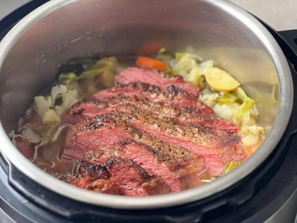 sliced corned beef in a pressure cooker with cabbage, carrots, and potatoes