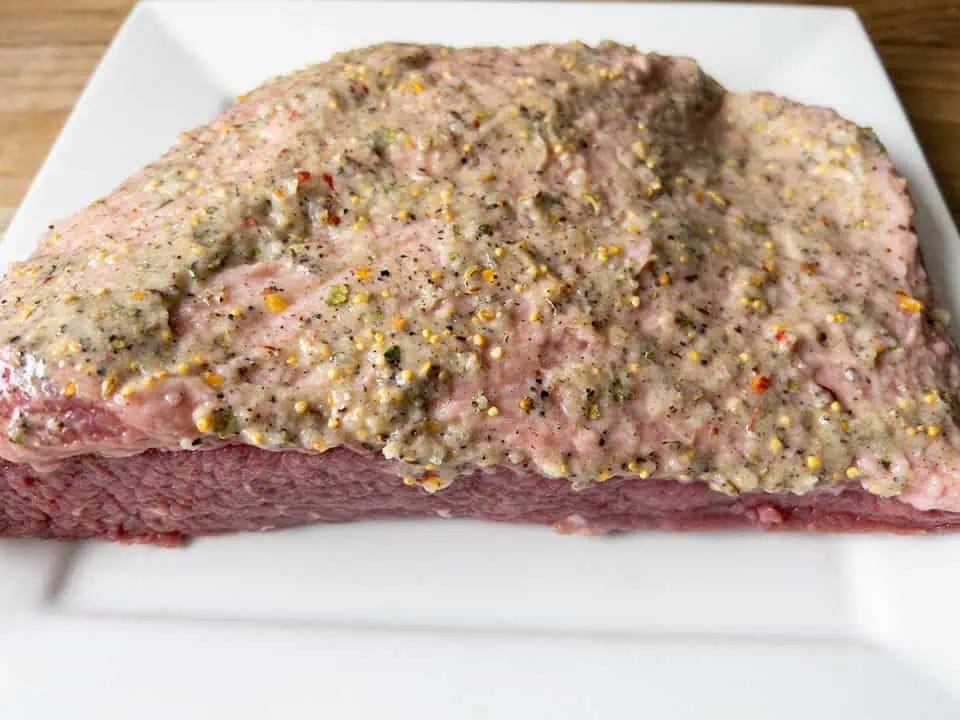 Uncooked corned beef brisket covered with garlic/spice blend on a white plate.