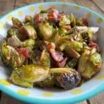 Maple Bacon Brussels Sprouts in a white bowl with yellow polka dots sitting on wood table.