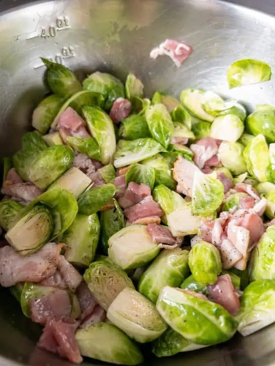 Uncooked maple bacon Brussels sprouts tossed in large mixing bowl.