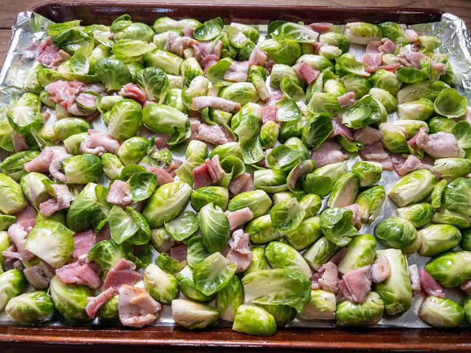 Uncooked maple bacon Brussels sprouts spread out on baking sheet lined with foil.