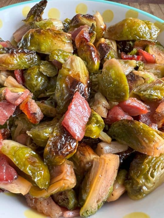 Maple Bacon Brussels Sprouts in a white bowl with yellow polka dots sitting on wood table.