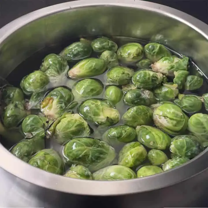 Large stainless steel bowl with Brussels sprouts soaking in water.