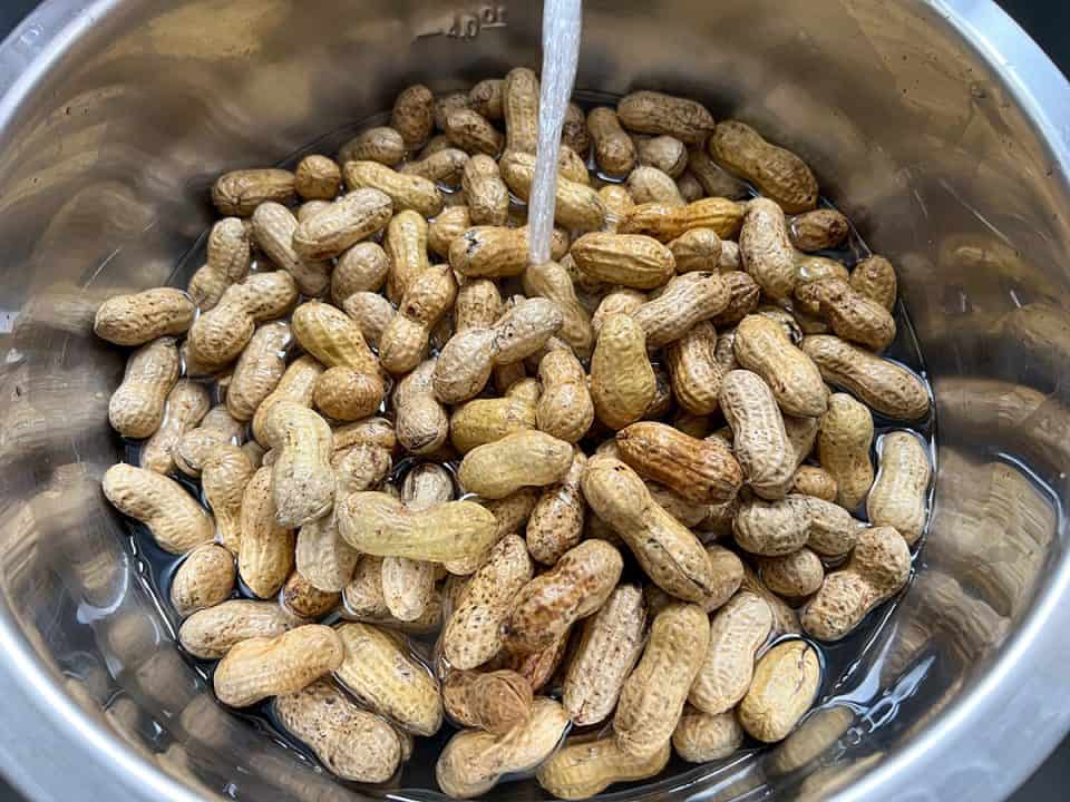 Raw peanuts in a large bowl under running water.