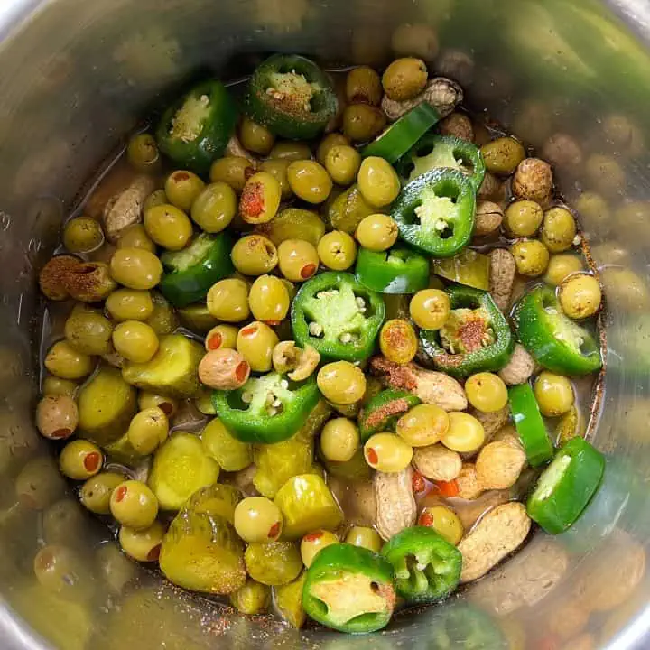 Raw peanuts with pickles, jalapenos, and olives in Instant Pot topped with cajun seasoning.