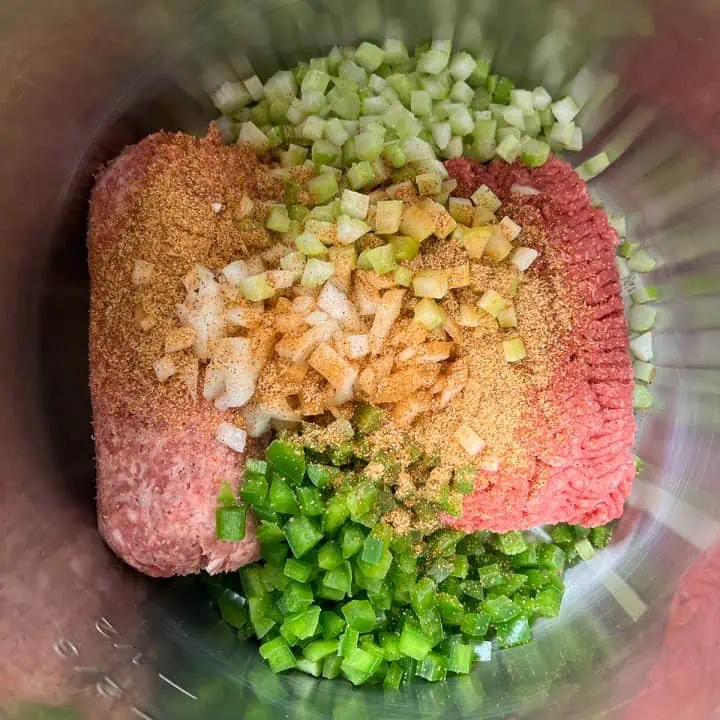 Uncooked ground beef and sausage topped with diced onions, celery, bell peppers, and creole seasoning.