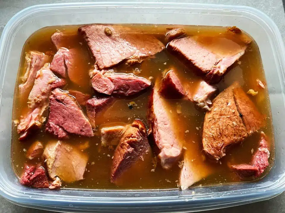 Ham with broth in a plastic storage container.