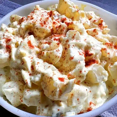 Instant Pot potato salad toped with paprika in a white bowl with a gray and blue background.