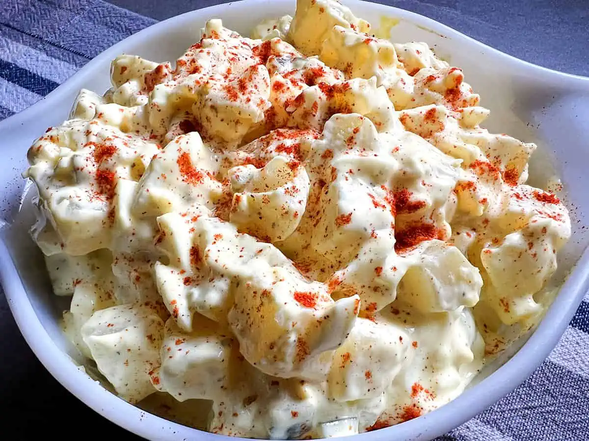 Instant Pot potato salad toped with paprika in a white bowl with a gray and blue background.