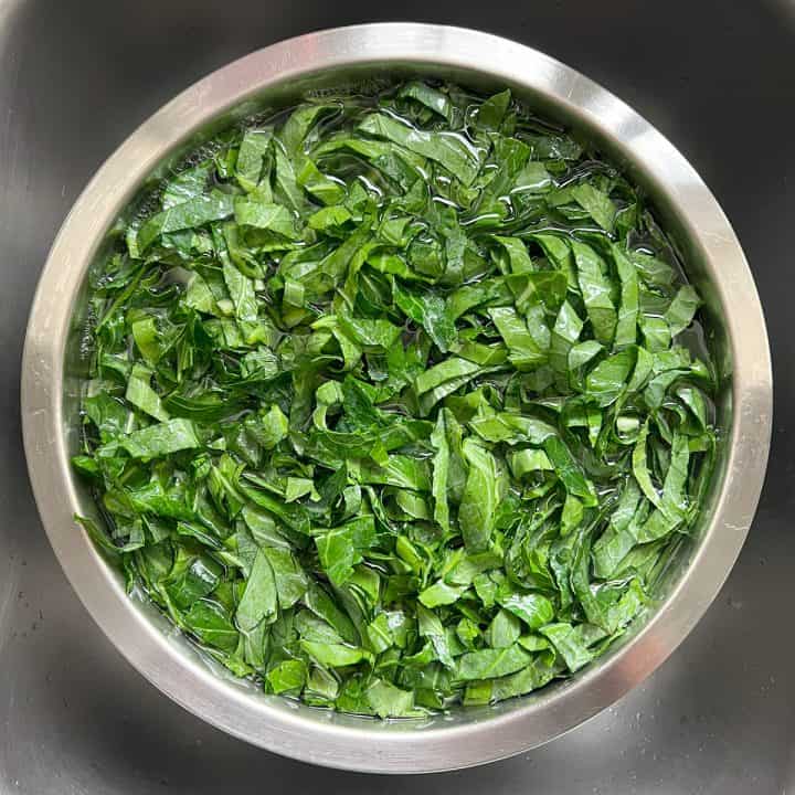 Shredded collard greens in a large stainless steel bowl.
