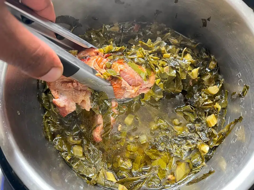 Removing smoked turkey wing from a pot of collard greens.