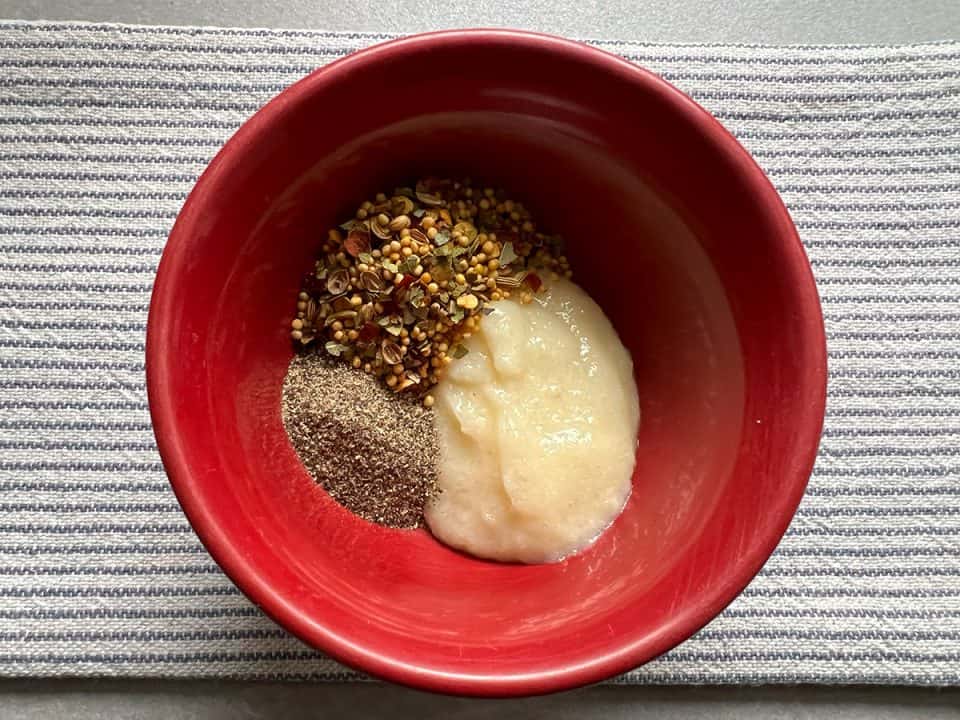 Garlic paste, black pepper, and pickling spices in a small red bowl.