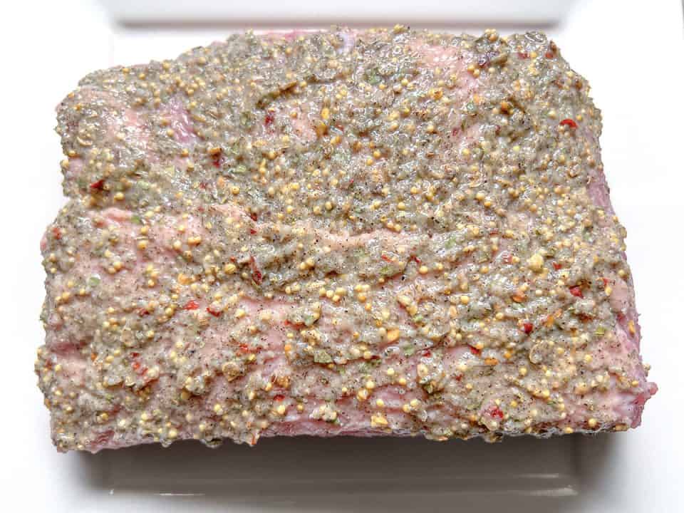 Corned beef brisket topped with a spice and garlic paste on a white plate.