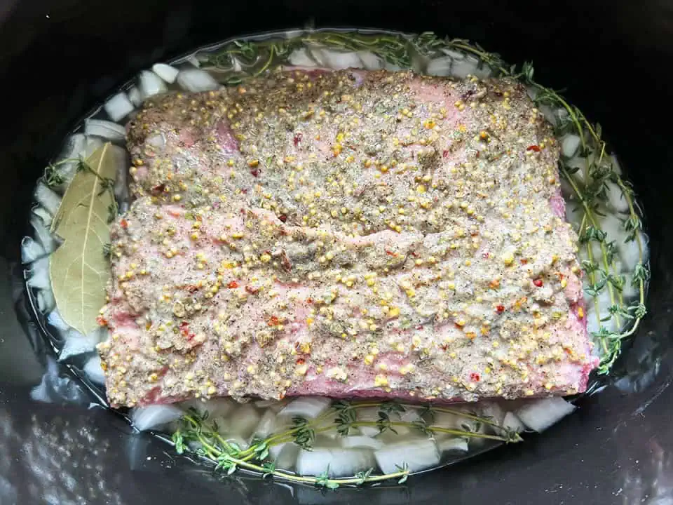 Corned beef brisket in a slow cooker with onions, thyme, and a bay leaf.
