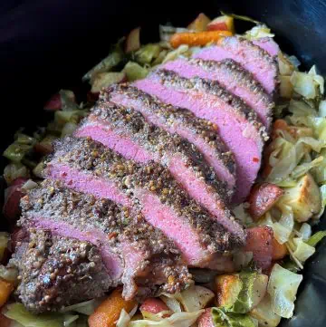 Sliced corned beef brisket on top of cabbage, potatoes, and carrots in a slow cooker.