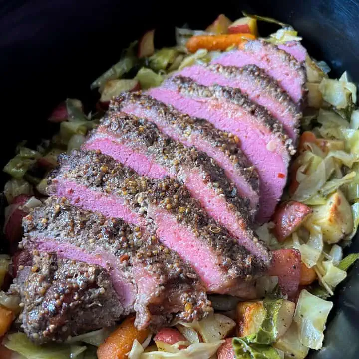 Sliced corned beef brisket on top of cabbage, potatoes, and carrots in a slow cooker.